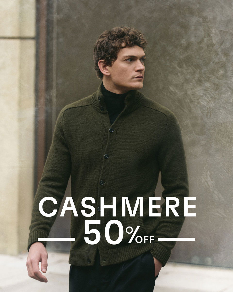 Mann mit lockigem Haar trägt olivgrüne Cashmere-Strickjacke, schwarzes Shirt, Text: Cashmere 50% Rabatt, urbaner Hintergrund.