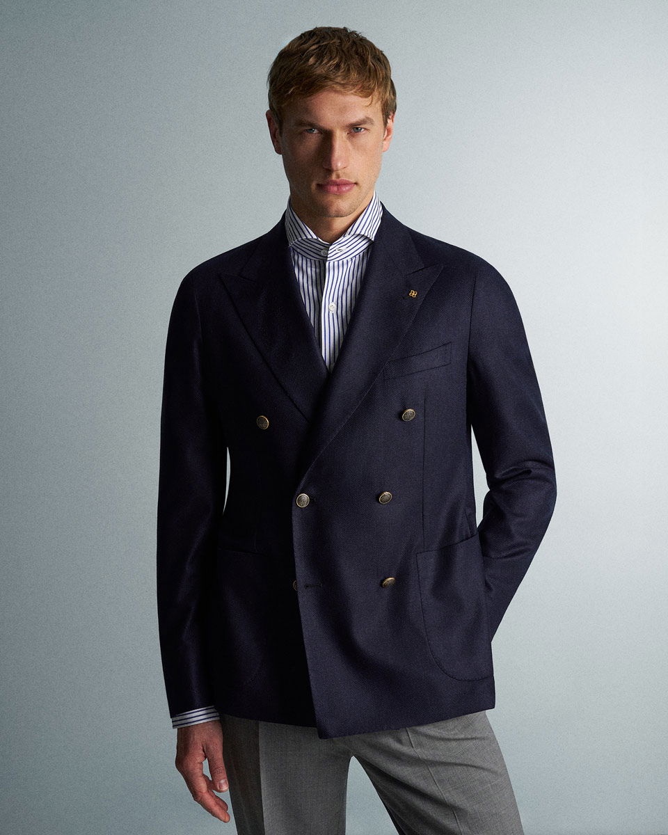 Man wearing a dark navy double-breasted blazer with gold buttons, a blue and white striped shirt, and gray trousers.