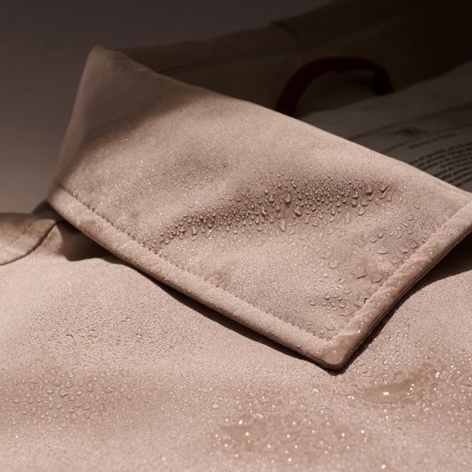 Beiger Hemdkragen mit Wassertropfen, die die wasserabweisende Oberfläche des Stoffes zeigen, Nahaufnahme bei gedämpftem Licht.