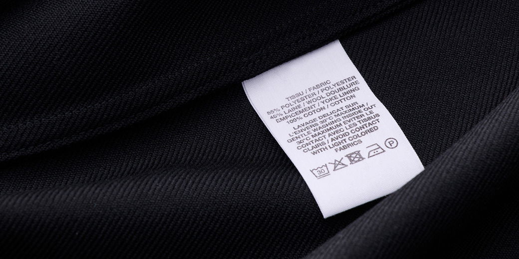 Weißes Pflegeetikett mit Text und Waschsymbole auf schwarzem Stoff, Detailaufnahme der Textilkennzeichnung.