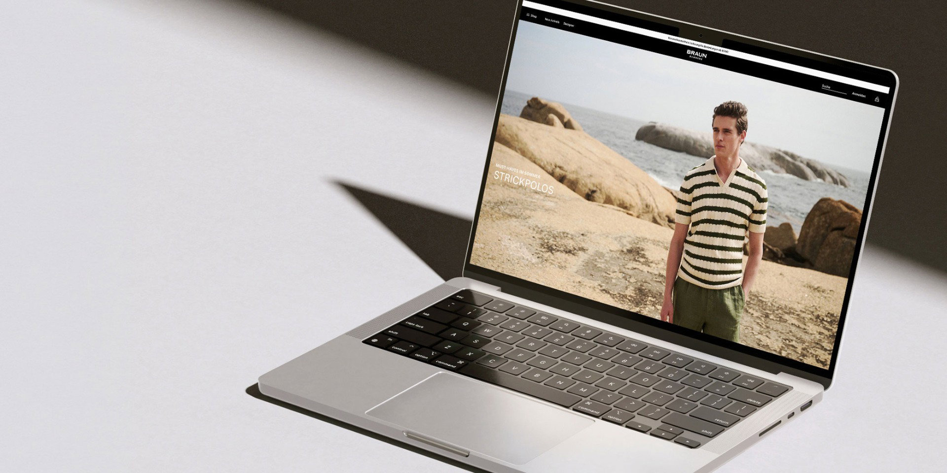 Laptop auf hellem Untergrund mit geöffneter Webseite, die einen Mann in gestreiftem Strickpolo vor Felsen und Meer zeigt.