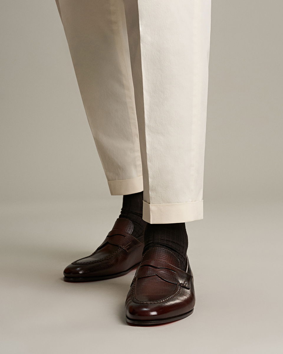 Anschnitt einer getragenen Herrenhose in beige mit Turn-Up-Krempelung, kombiniert zu braunen Penny Loafern Anschnitt einer getragenen Herrenhose in beige mit Turn-Up-Krempelung, kombiniert zu braunen Penny Loafern