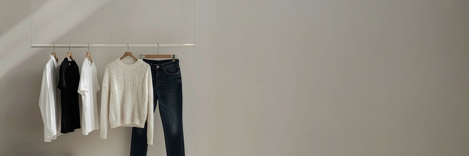 An Kleiderstange hängend: weißes Hemd, schwarzes T-Shirt, weißes T-Shirt, cremefarbener Pullover mit Zopfmuster, blaue Jeans. An Kleiderstange hängend: weißes Hemd, schwarzes T-Shirt, weißes T-Shirt, cremefarbener Pullover mit Zopfmuster, blaue Jeans.