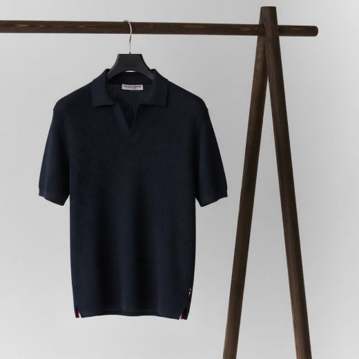 Dunkelblaues, kurzärmliges Strick-Poloshirt für Herren an einer dunklen Holzkleiderstange hängend vor weißem Hintergrund.