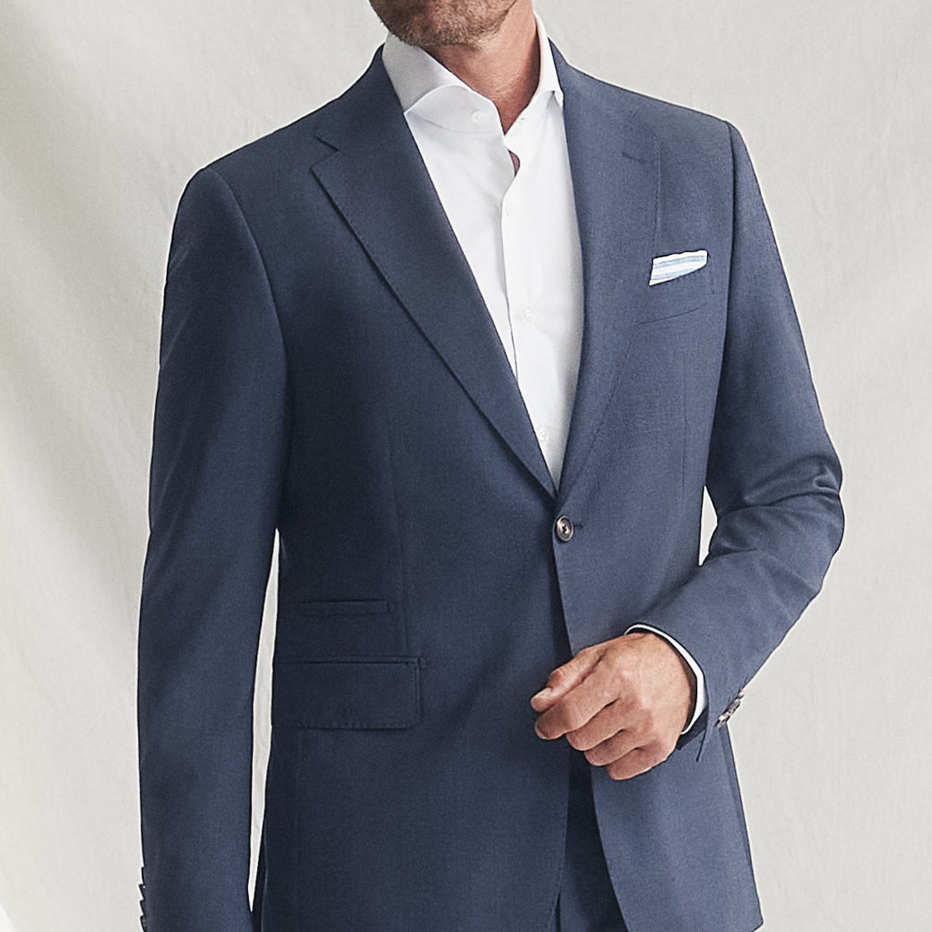Mann trägt dunkelblaues Sakko mit weißem Businesshemd und weißem Einstecktuch, Halbkörperaufnahme ohne Kopf.