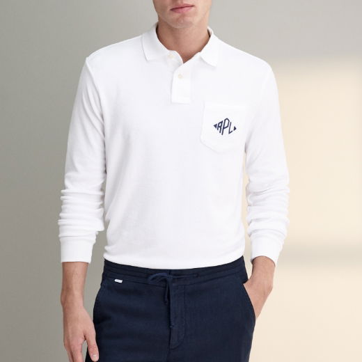 Mann trägt weißes Langarm-Poloshirt mit Brusttasche und dunkelblaue Hose, Hände teils in den Hosentaschen.