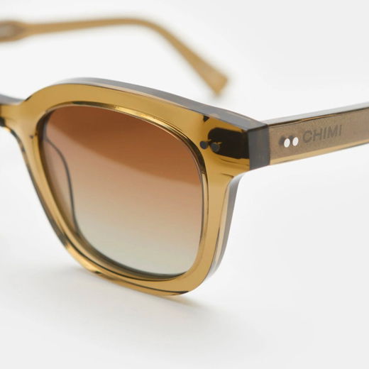 Anschnitt einer transparent-olivfarbenen Sonnenbrille mit braun getönten Gläsern und Markenlogo 'CHIMI' am Bügel.