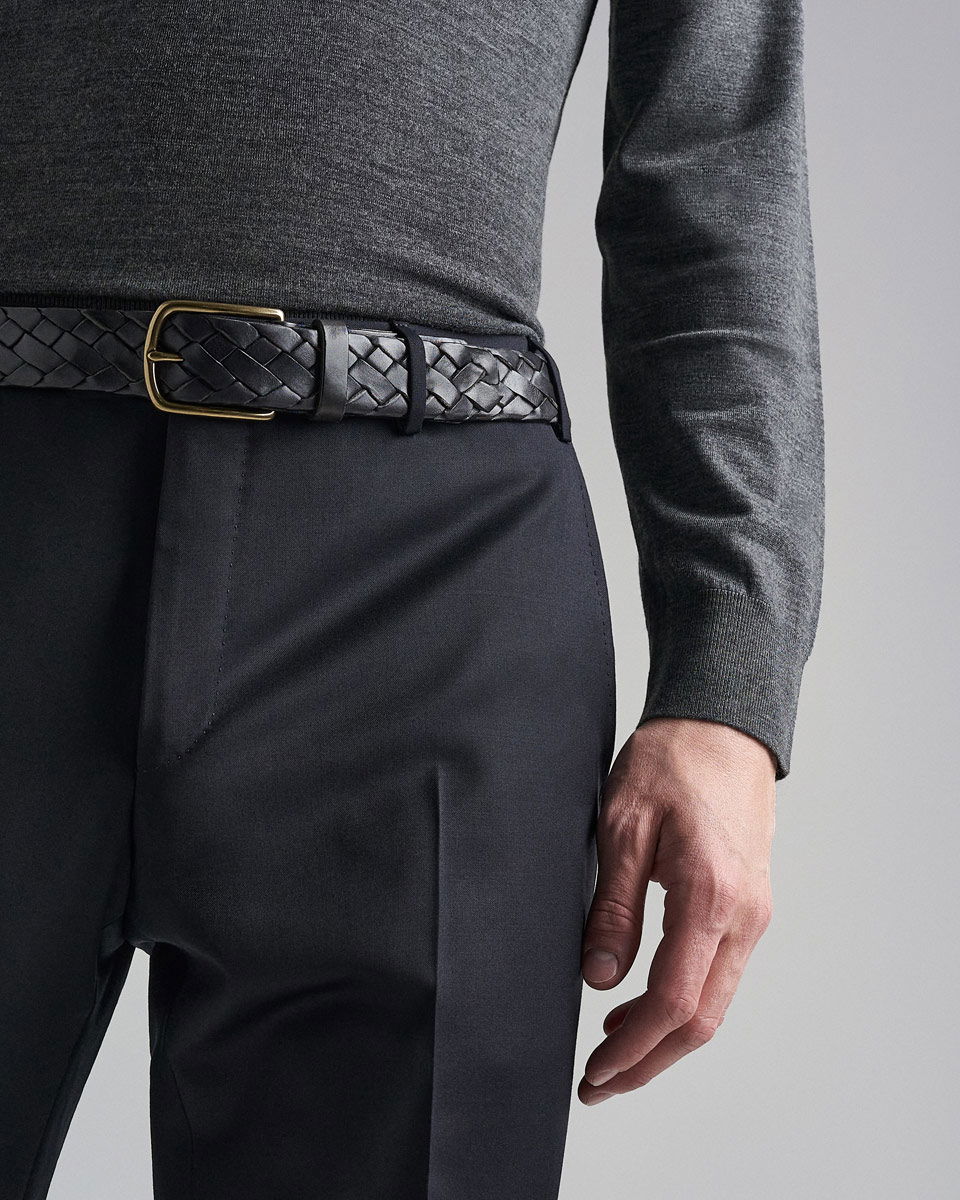 Anschnitt eines Mannes mit navyblauer Hose, grauem Longsleeve und schwarzem geflochtenem Ledergürtel mit goldener Schnalle.