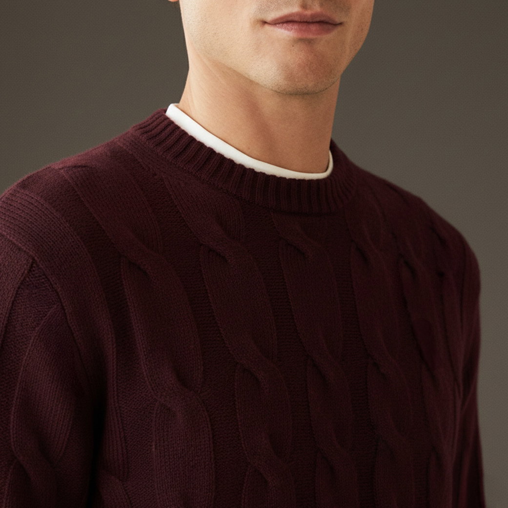 Mann mit bordeauxrotem Zopfstrick-Rundhalspullover über weißem Shirt, angeschnittener Oberkörper vor grauem Hintergrund. Mann mit bordeauxrotem Zopfstrick-Rundhalspullover über weißem Shirt, angeschnittener Oberkörper vor grauem Hintergrund.