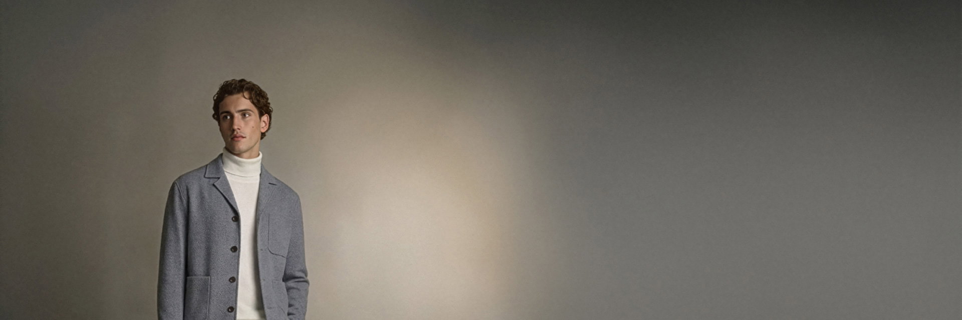 Junger Mann mit lockigem Haar trägt graues Overshirt über weißem Rollkragenpullover vor neutralem Hintergrund. Junger Mann mit lockigem Haar trägt graues Overshirt über weißem Rollkragenpullover vor neutralem Hintergrund.