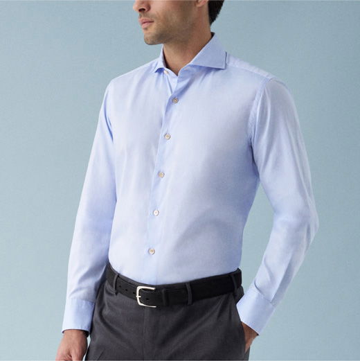 Mann trägt hellblaues Hemd mit Knöpfen, dunkelblaue Hose und schwarzen Gürtel, vor hellblauem Hintergrund.