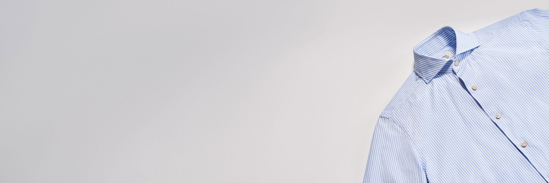 Blau-weiß gestreiftes Herrenhemd mit Knöpfen und Kragen, flach auf hellem Hintergrund liegend, von oben fotografiert. Blau-weiß gestreiftes Herrenhemd mit Knöpfen und Kragen, flach auf hellem Hintergrund liegend, von oben fotografiert.