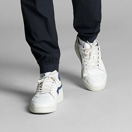 Anschnitt einer getragenen navyblauen Cargohose für Herren mit weißen Sneakern und grauen Socken auf grauem Hintergrund.