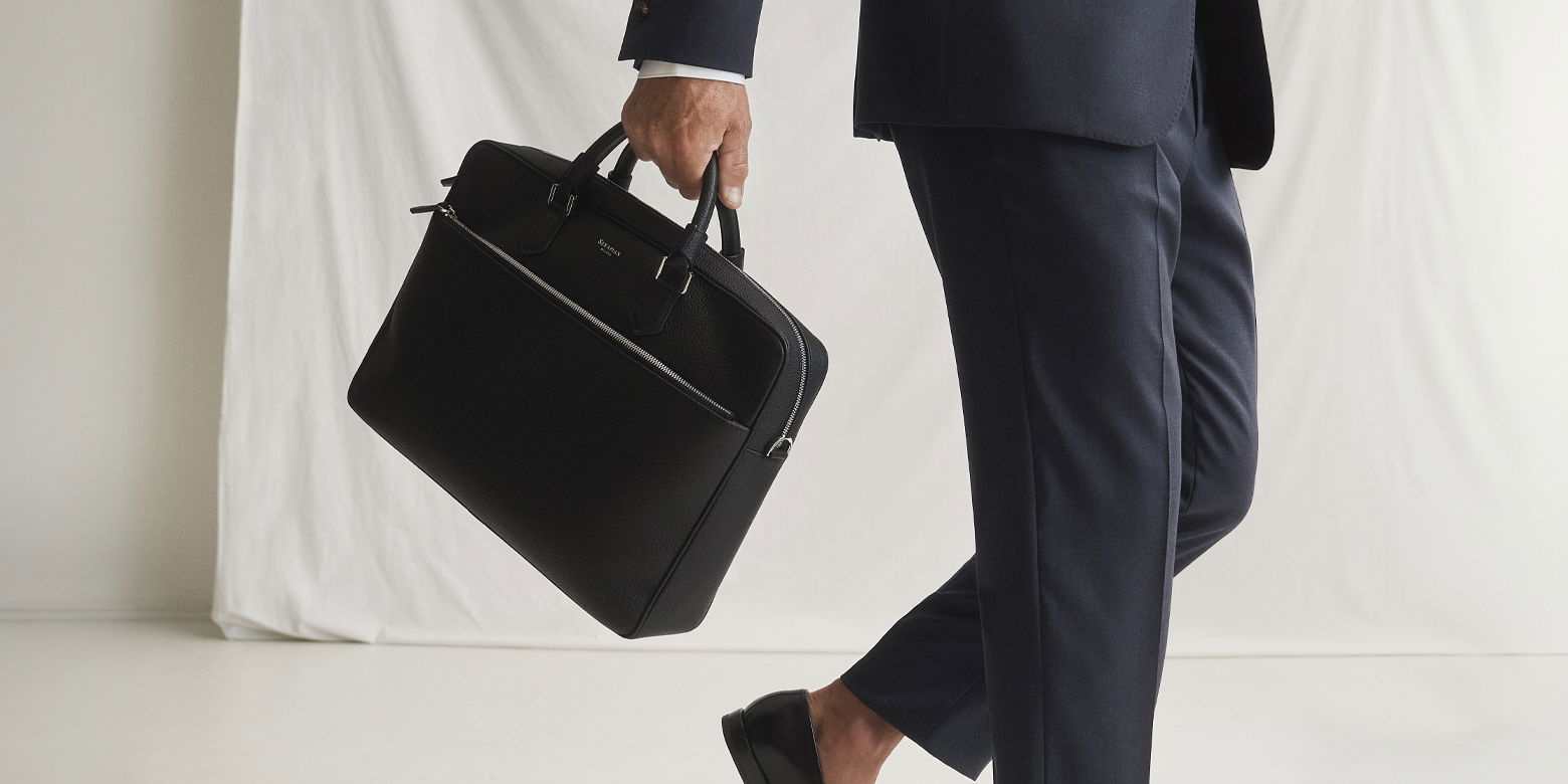 Anschnitt eines laufenden Mannes im dunkelblauen Anzug, der eine schwarze Aktentasche und schwarze Loafer trägt.