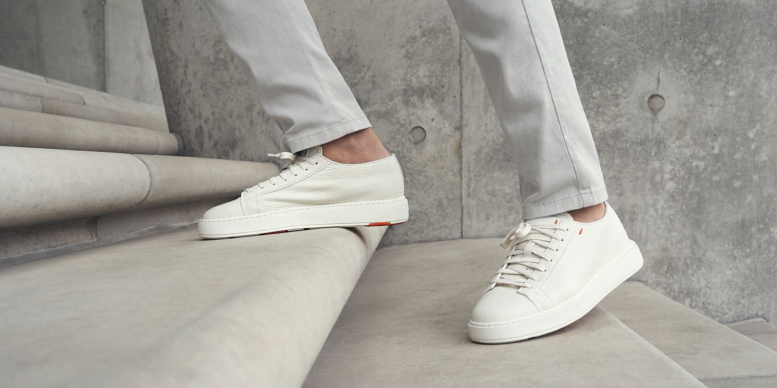 Herrenbeine mit hellgrauer Hose und weißen Sneakern steigen auf eine helle Treppe aus Beton.