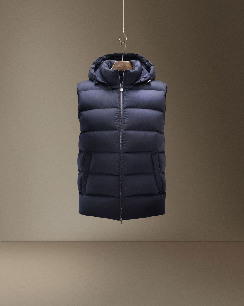 Dunkelblaue, wattierte Daunenweste mit Kapuze, Reißverschluss und zwei seitlichen Taschen, auf Bügel hängend.