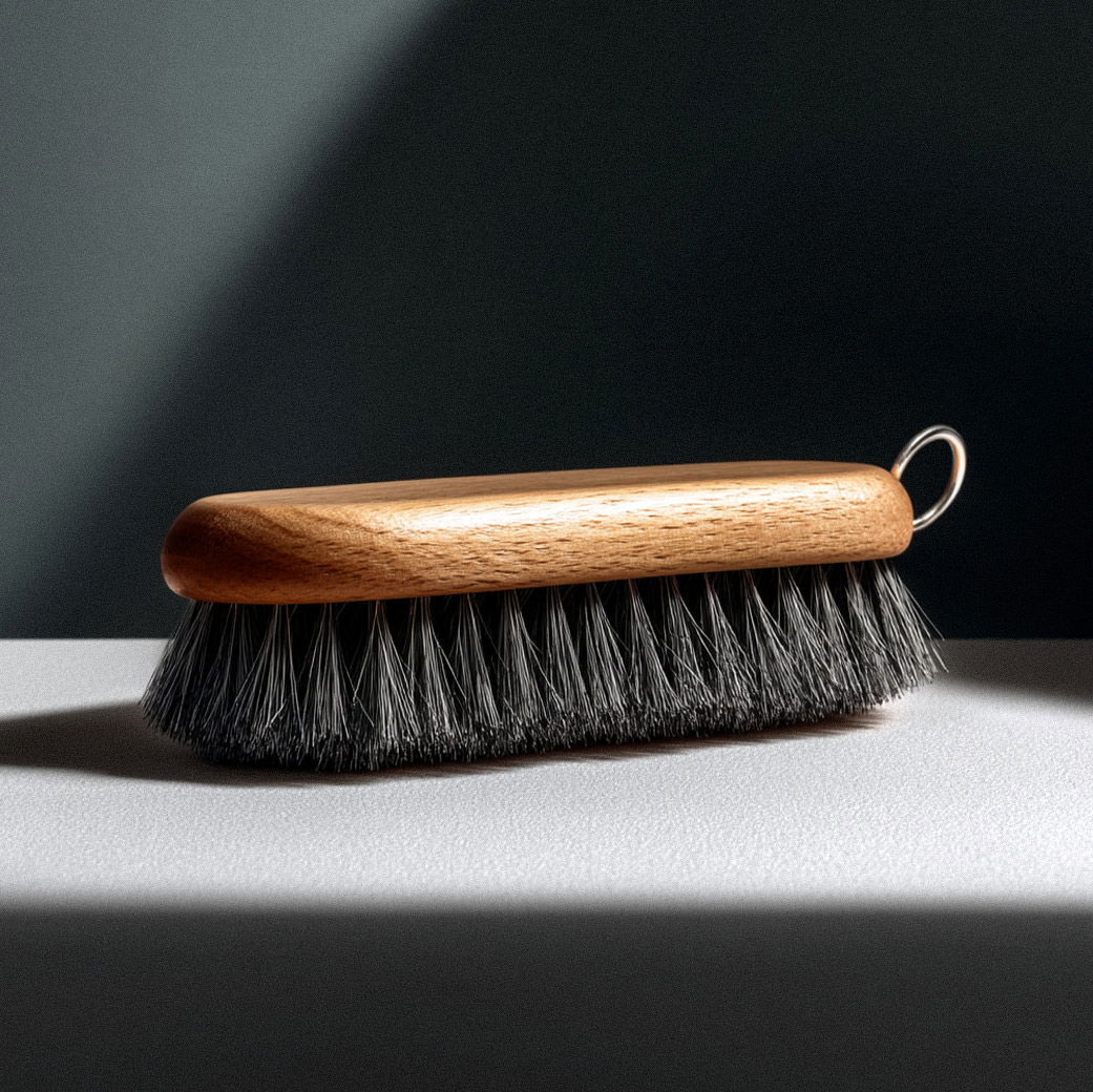 Cordbürste mit hellem Holzgriff, schwarzen Borsten und Metallöse liegt auf hellem Tisch vor dunklem Hintergrund. Cordbürste mit hellem Holzgriff, schwarzen Borsten und Metallöse liegt auf hellem Tisch vor dunklem Hintergrund.