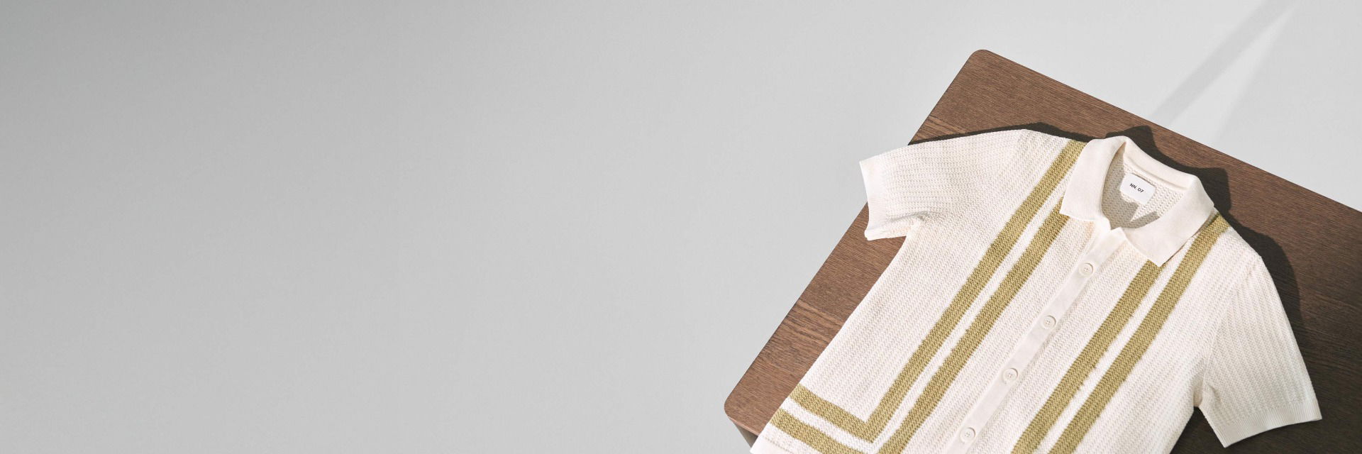 Cremefarbenes Strickhemd mit kurzen Ärmeln und grünen Streifen, liegend auf einem braunen Holztisch. Cremefarbenes Strickhemd mit kurzen Ärmeln und grünen Streifen, liegend auf einem braunen Holztisch.