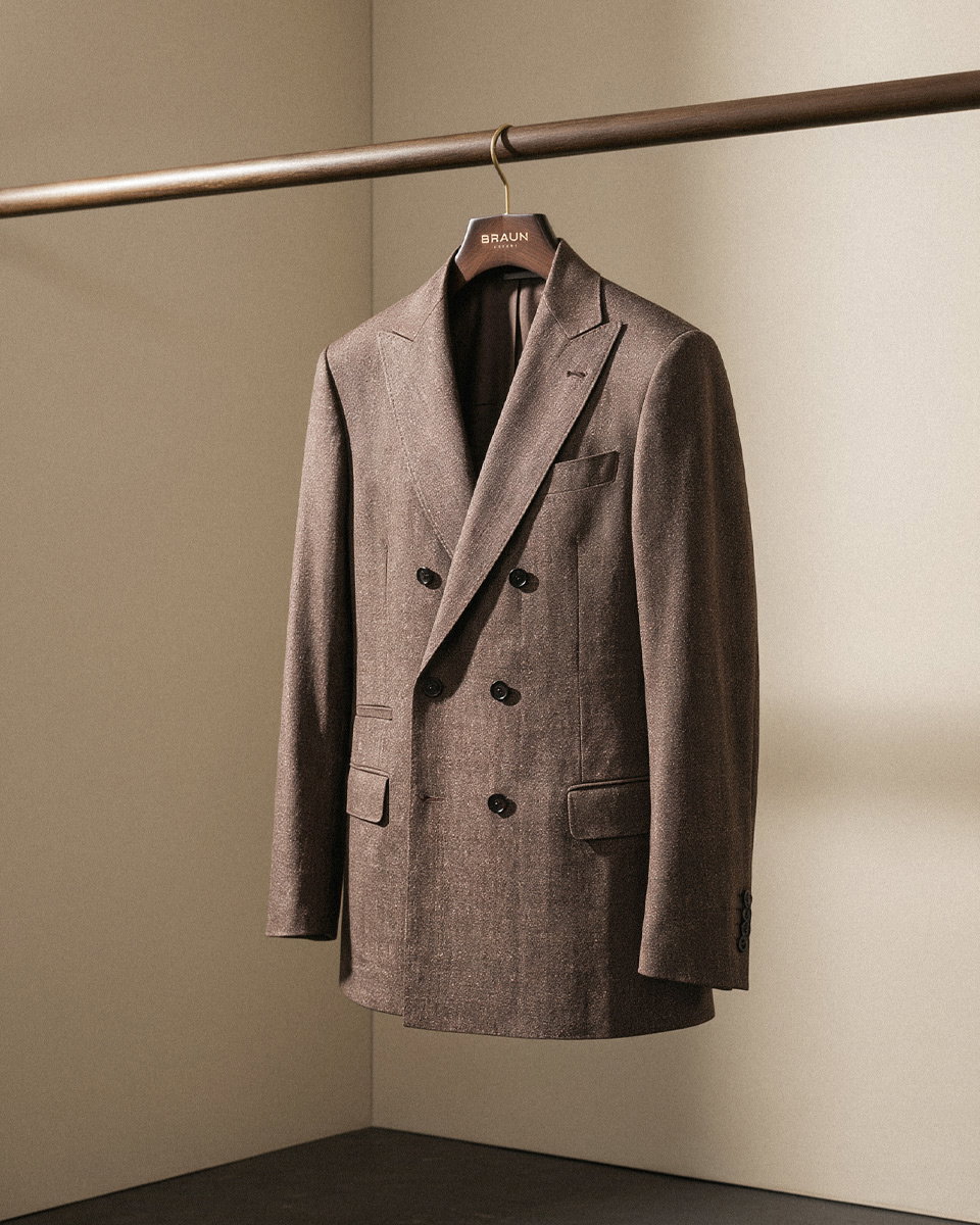 Dunkelbraunes, doppelreihiges Leinensakko auf einem Holzkleiderbügel an einer braunen Kleiderstange hängend.