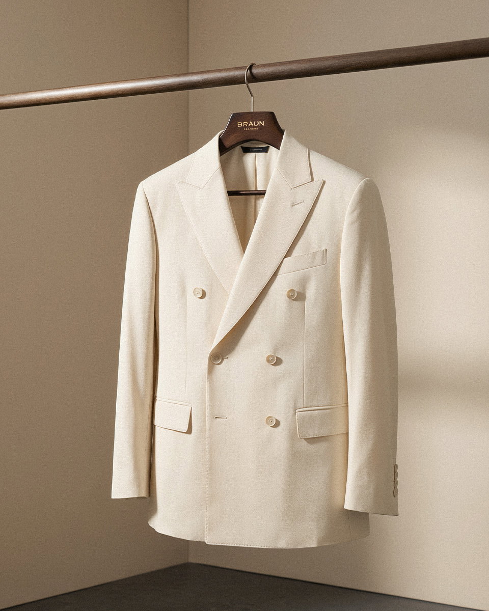 Weißes Doppelreiher-Sakko aus Schurwolle an Holzkleiderbügel auf brauner Kleiderstange hängend.