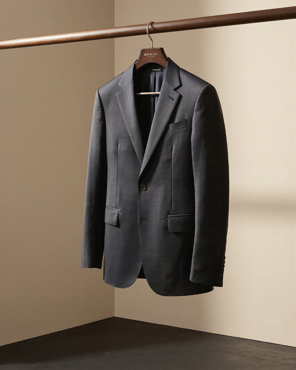 Dunkelgraues Sakko aus Merinowolle hängt an einem Holzkleiderbügel an einer Kleiderstange vor beiger Wand.