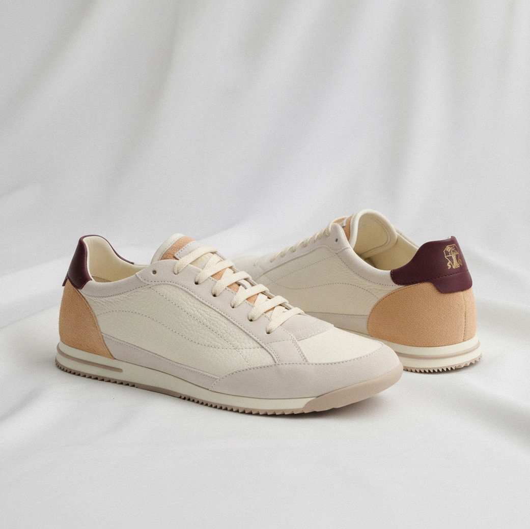 Creme-beigefarbene Sneaker mit roten und orangenen Details, weißen Schnürsenkeln auf hellem Stoff, Paaransicht.