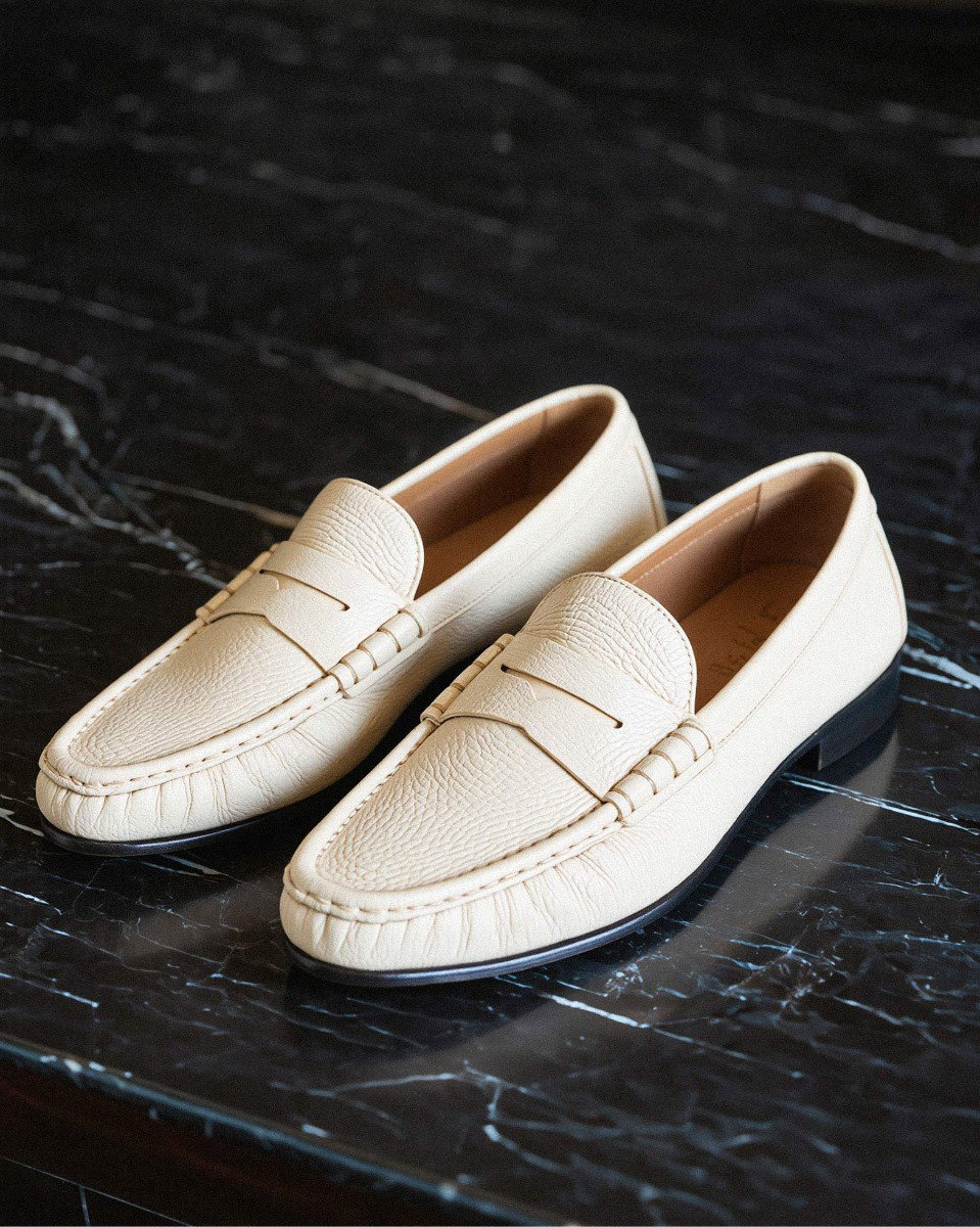 Cremefarbene Herren-Leder-Loafer mit Penny Strap auf schwarzem, marmoriertem Untergrund, seitliche Ansicht. Cremefarbene Herren-Leder-Loafer mit Penny Strap auf schwarzem, marmoriertem Untergrund, seitliche Ansicht.
