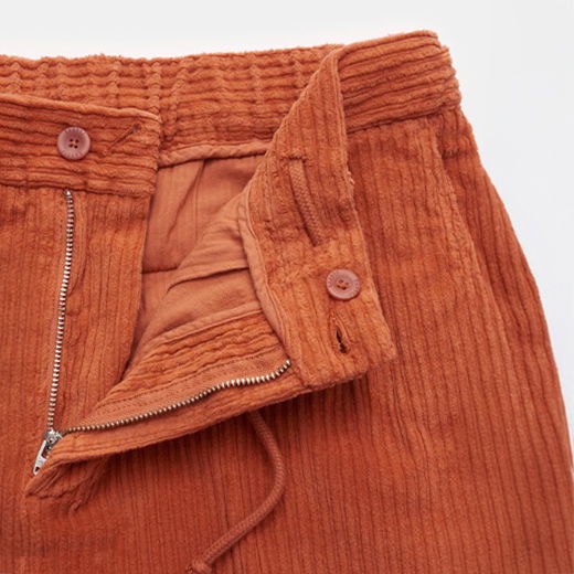 Herren-Cordhose in Orange, Detailansicht mit offenem Reißverschluss, teilelastischem Bund, Tunnelzug und Knöpfen aus Cordstoff.