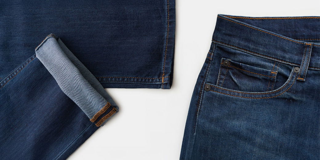 Dunkelblaue Herren-Jeans mit sichtbaren orangefarbenen Nähten, Hosentaschen und umgeschlagenem Beinabschluss.