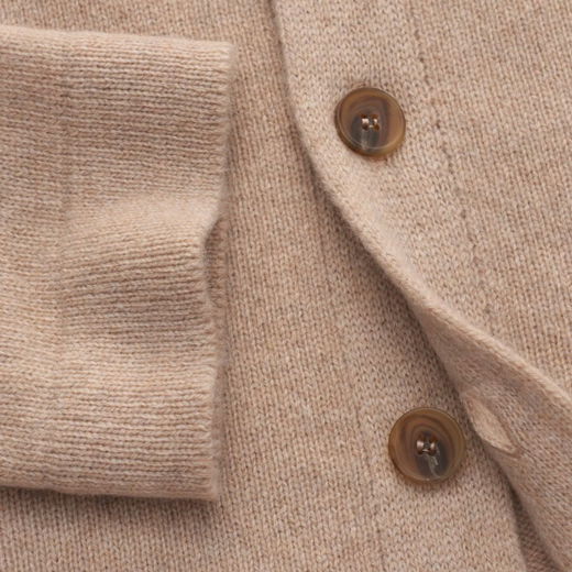 Beige Woll-Cardigan mit geripptem Bündchen und zwei braunen Knöpfen, Detailaufnahme von Ärmel und Knopfleiste. Beige Woll-Cardigan mit geripptem Bündchen und zwei braunen Knöpfen, Detailaufnahme von Ärmel und Knopfleiste.