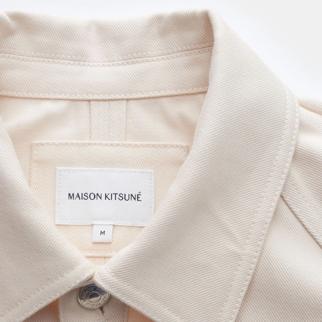 Beiger Kragen einer Herren-Jeansjacke mit weißem Designerlabel 'Maison Kitsuné' und Metallknopf in Größe M.