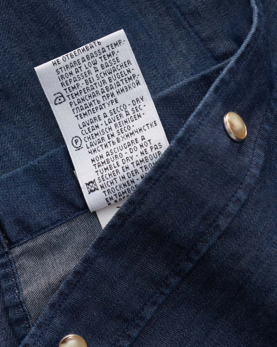 Pflegeetikett eines dunkelblauen Herrenhemds mit Bügelhinweisen und Waschsymbolen, detailreich und gut lesbar.