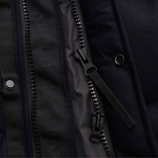 Detailaufnahme eines schwarzen Reißverschlusses und Stoffdetails einer Herren-Outdoorweste mit Logo und Knopfverschluss.