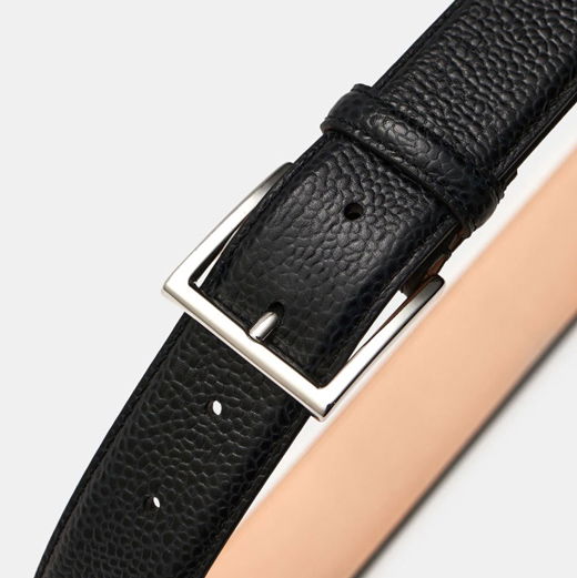 Schwarzer Ledergürtel mit genarbter Oberfläche und silberner rechteckiger Metallschließe, Nahaufnahme vor hellem Hintergrund. Schwarzer Ledergürtel mit genarbter Oberfläche und silberner rechteckiger Metallschließe, Nahaufnahme vor hellem Hintergrund.