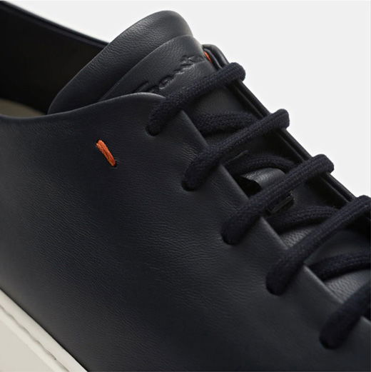 Nahaufnahme eines navyblauen Herrensneakers aus Leder mit schwarzen Schnürsenkeln und Prägung auf der Schuhlasche. Nahaufnahme eines navyblauen Herrensneakers aus Leder mit schwarzen Schnürsenkeln und Prägung auf der Schuhlasche.