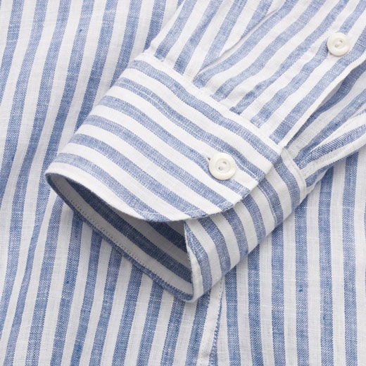 Blau-weiß gestreifte Sportmanschette eines Herrenhemds aus leichtem Leinenstoff, mit weißem Knopf und feiner Naht. Blau-weiß gestreifte Sportmanschette eines Herrenhemds aus leichtem Leinenstoff, mit weißem Knopf und feiner Naht.