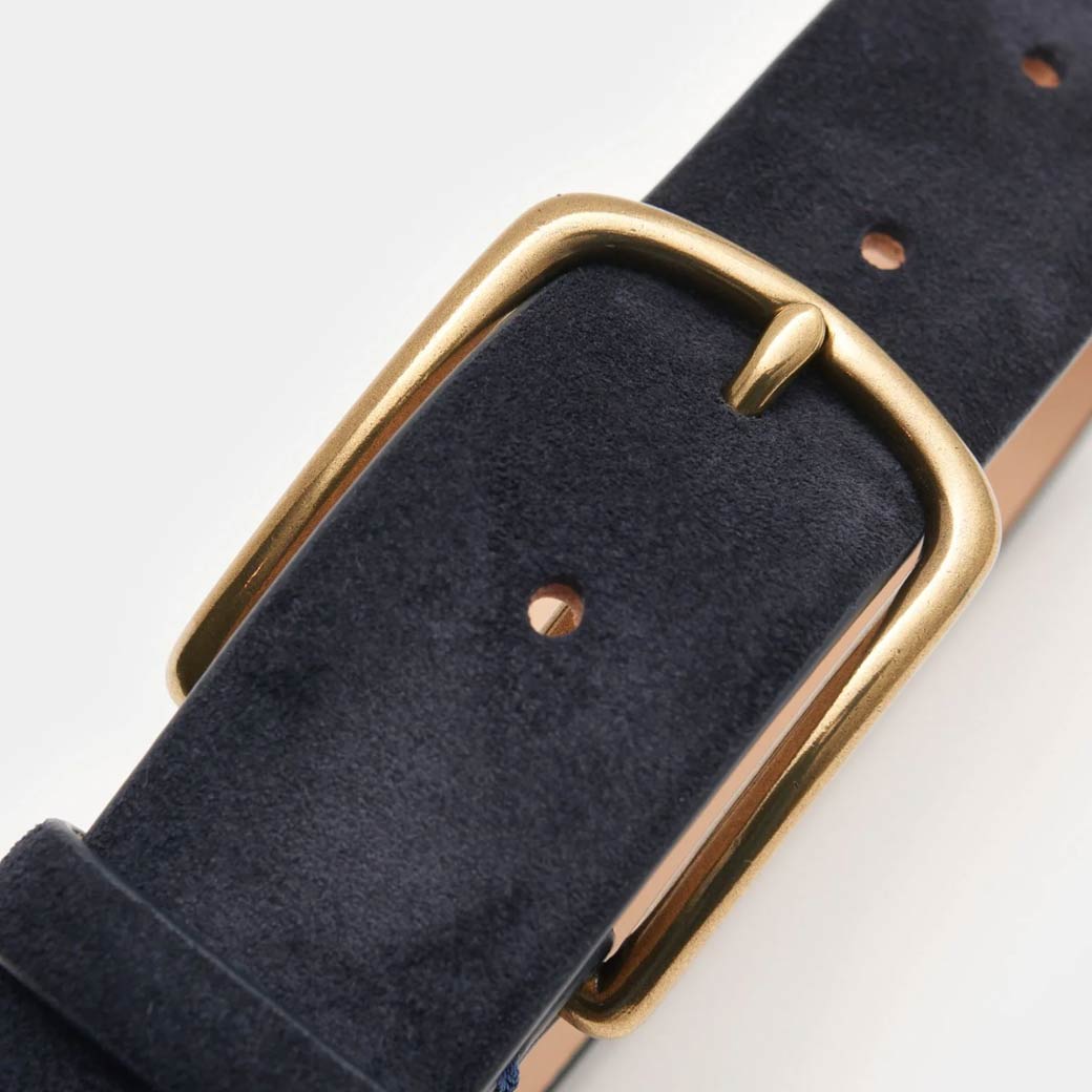 Dunkelblauer Veloursledergürtel mit goldener, rechteckiger Metallschnalle und drei Lochungen auf hellem Hintergrund. Dunkelblauer Veloursledergürtel mit goldener, rechteckiger Metallschnalle und drei Lochungen auf hellem Hintergrund.