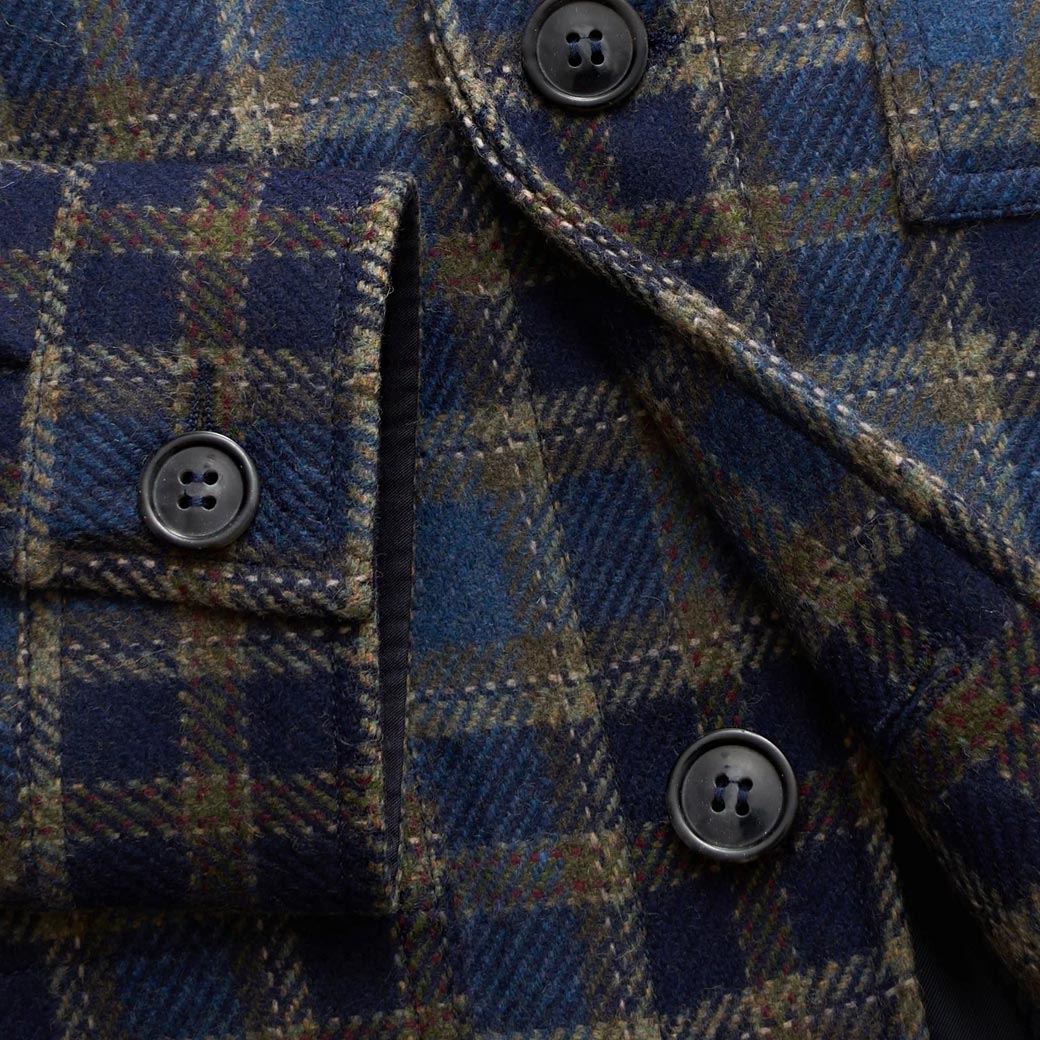 Detailansicht der Knopfleiste und Manschette einer blau-braun karierten Herrenjacke aus Wollstoff. Detailansicht der Knopfleiste und Manschette einer blau-braun karierten Herrenjacke aus Wollstoff.