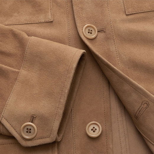 Detailaufnahme der Knopfleiste und eines Ärmels eines braunen Overshirts aus weichem Veloursleder mit vierlochigen Knöpfen.