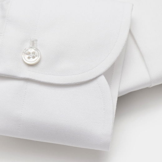Detailaufnahme einer weißen Manschette eines Herrenhemdes mit feinem Stoff, sauberer Naht und Perlmutt-Knopf.