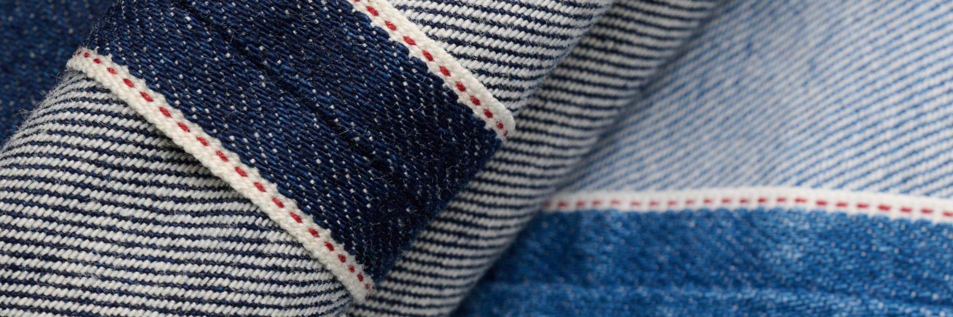 Detailaufnahme der roten Naht und blauen Webkante einer hochwertigen Selvedge-Denim-Herrenjeans aus Baumwolle. Detailaufnahme der roten Naht und blauen Webkante einer hochwertigen Selvedge-Denim-Herrenjeans aus Baumwolle.