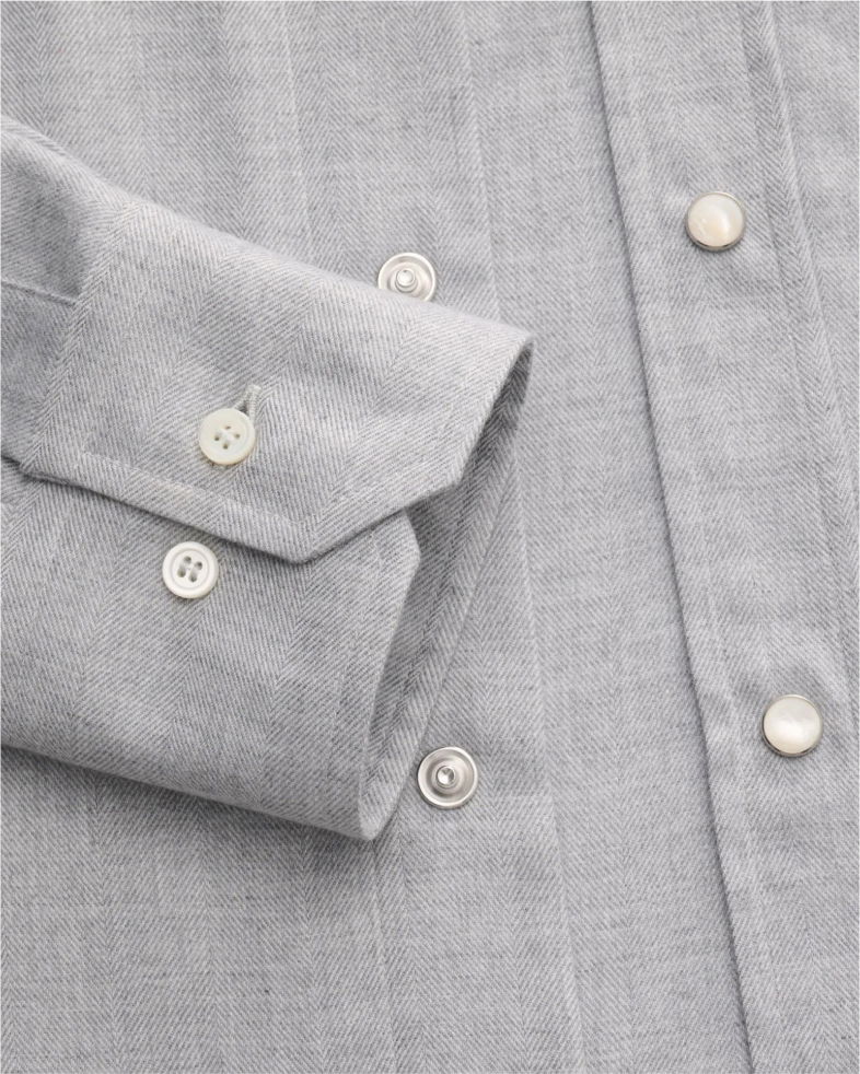 Detailaufnahme einer grauen Herrenhemd-Sportmanschette aus Fischgrät-Stoff mit weißen Knöpfen und Druckknöpfen. Detailaufnahme einer grauen Herrenhemd-Sportmanschette aus Fischgrät-Stoff mit weißen Knöpfen und Druckknöpfen.