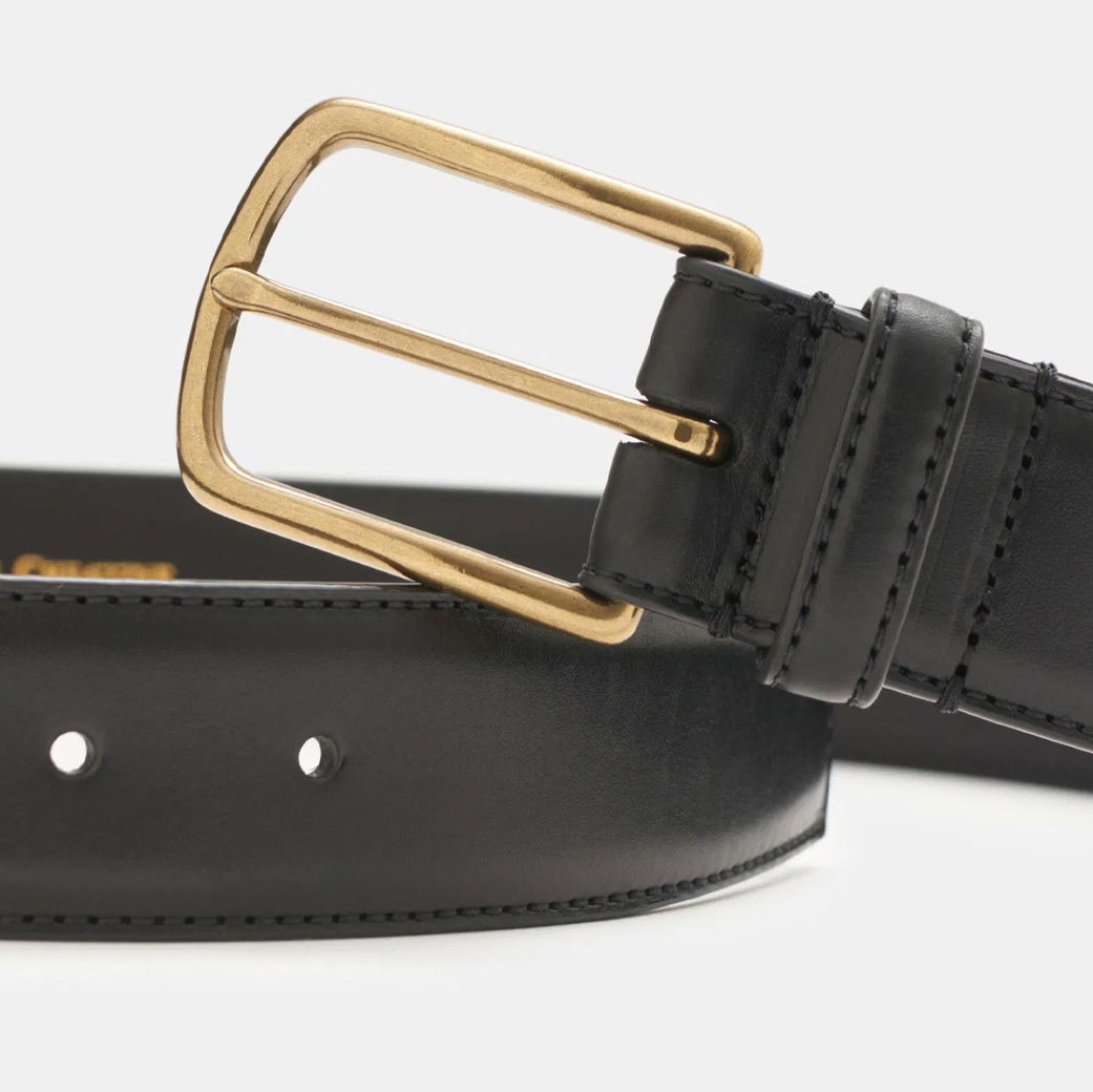 Detailaufnahme eines schwarzen Ledergürtels mit glatter Oberfläche und goldener Metallschnalle.