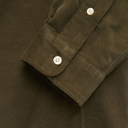 Detailaufnahme des Ärmels eines dunkelgrünen Cordhemdes mit weißen Knöpfen und sichtbarer Nahtstruktur. Detailaufnahme des Ärmels eines dunkelgrünen Cordhemdes mit weißen Knöpfen und sichtbarer Nahtstruktur.