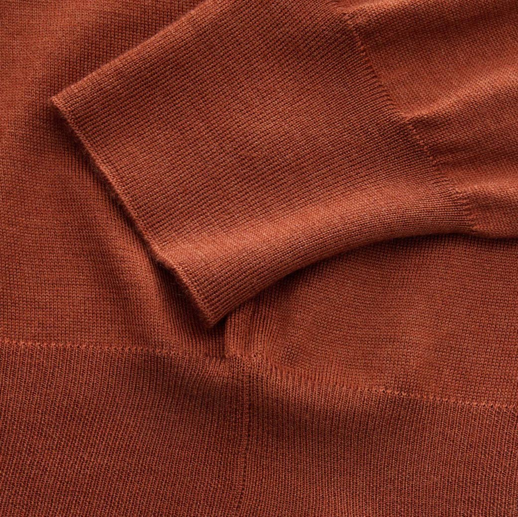 Detailaufnahme des terrakottafarbenen Feinstrick-Herrenpullovers mit Bündchen am Ärmel und feiner Strickstruktur.
