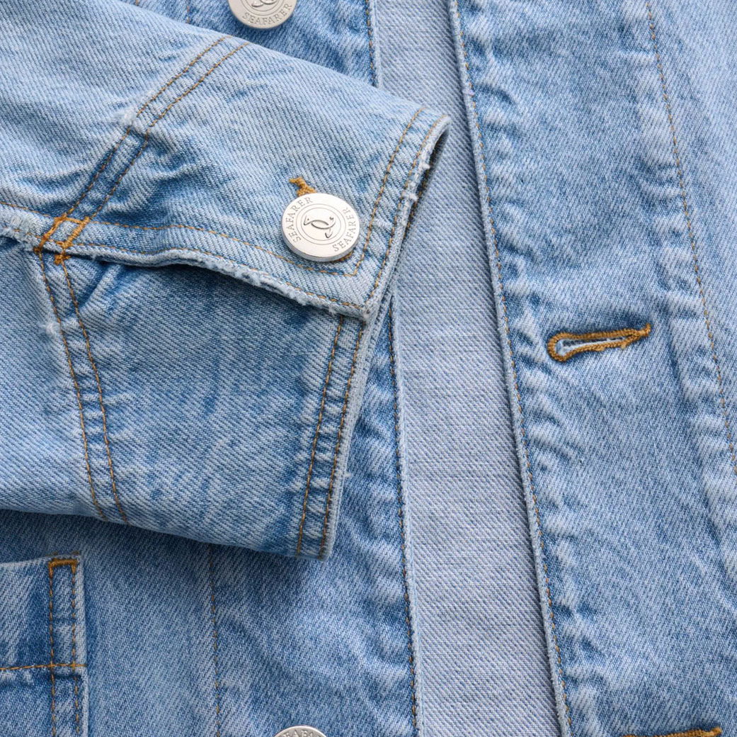 Detailaufnahme eines hellblauen Jeansjackenärmels mit silbernem Seafarer-Knopf und sichtbarer Knopfleiste.