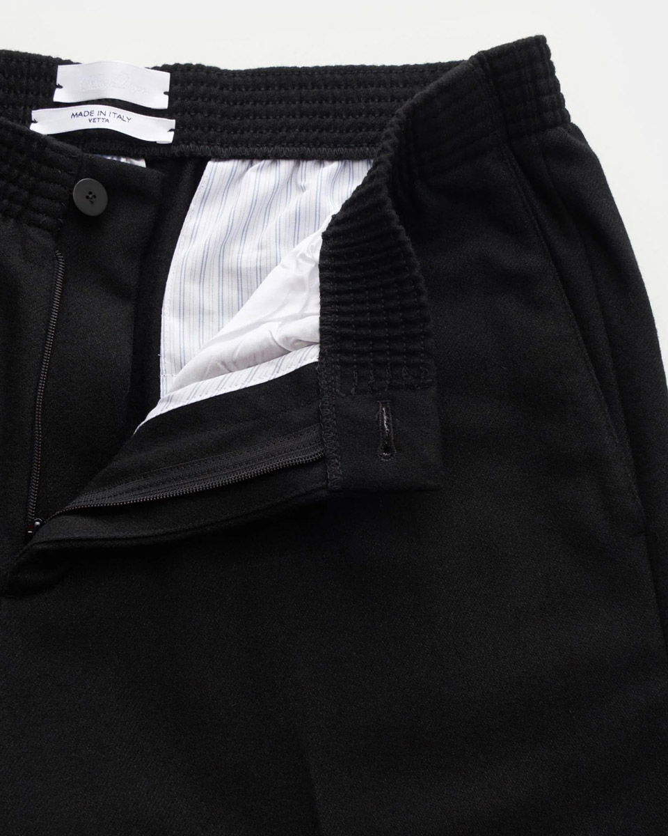 Detailaufnahme des geöffneten Bundes mit Reißverschluss und Knopf einer schwarzen Hose aus weichem Stoff.