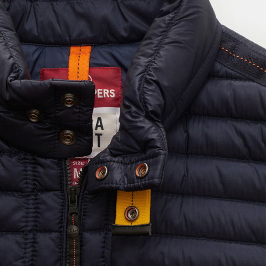 Dunkelblaue Daunenjacke mit Steppmuster, gelbem Knopfriegel am Kragen und sichtbar rotem Innenetikett. Dunkelblaue Daunenjacke mit Steppmuster, gelbem Knopfriegel am Kragen und sichtbar rotem Innenetikett.