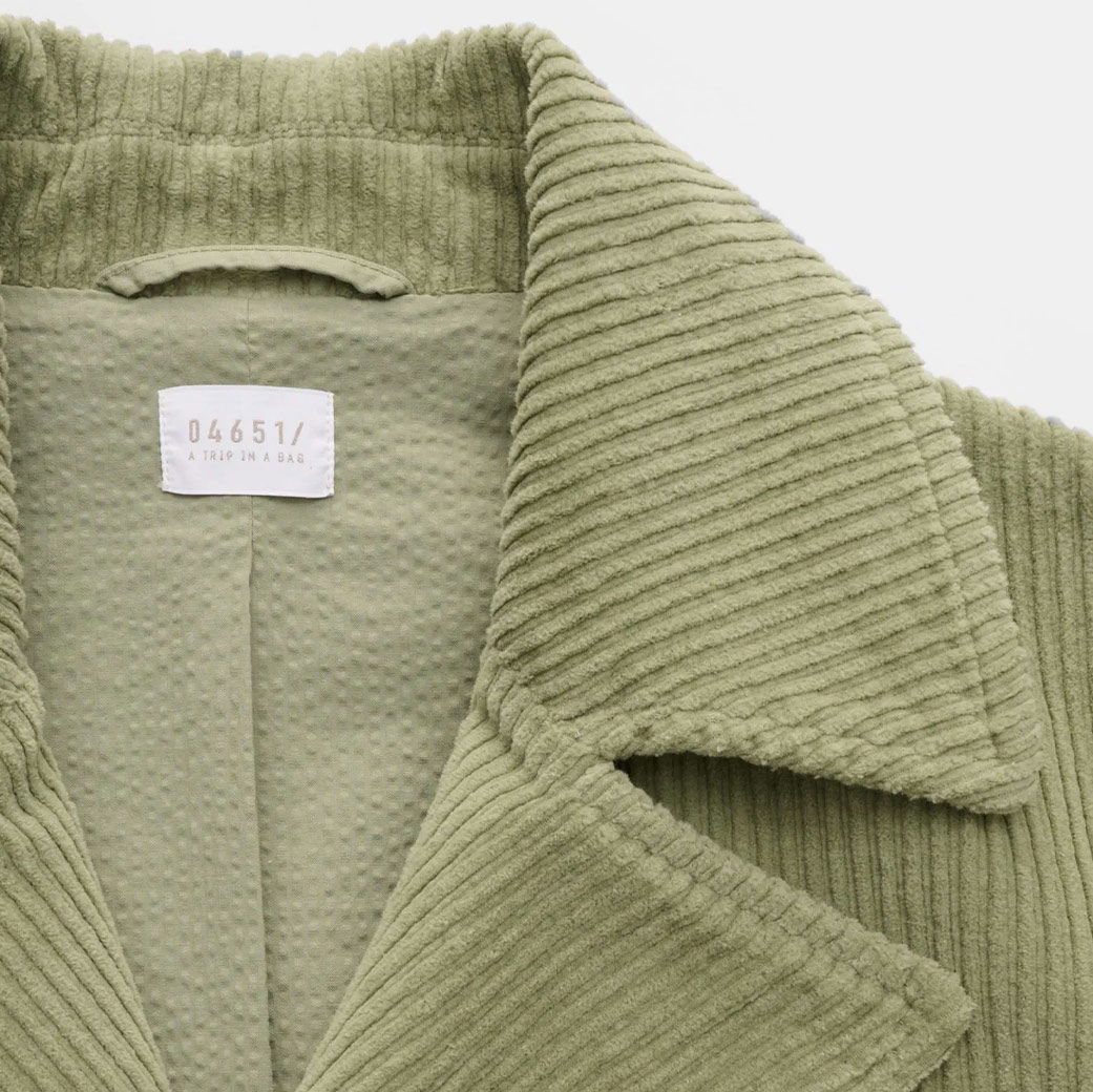 Detailaufnahme des Kragens einer hellgrünen Cordjacke für Herren mit sichtbarem weißen Designerlabel '04651 / A TRIP IN A BAG'.