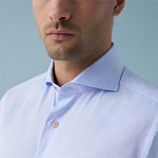 Nahaufnahme eines Mannes mit hellblauem Hemd, Fokus auf den klassischen Hemdkragen und die oberen Knöpfe.